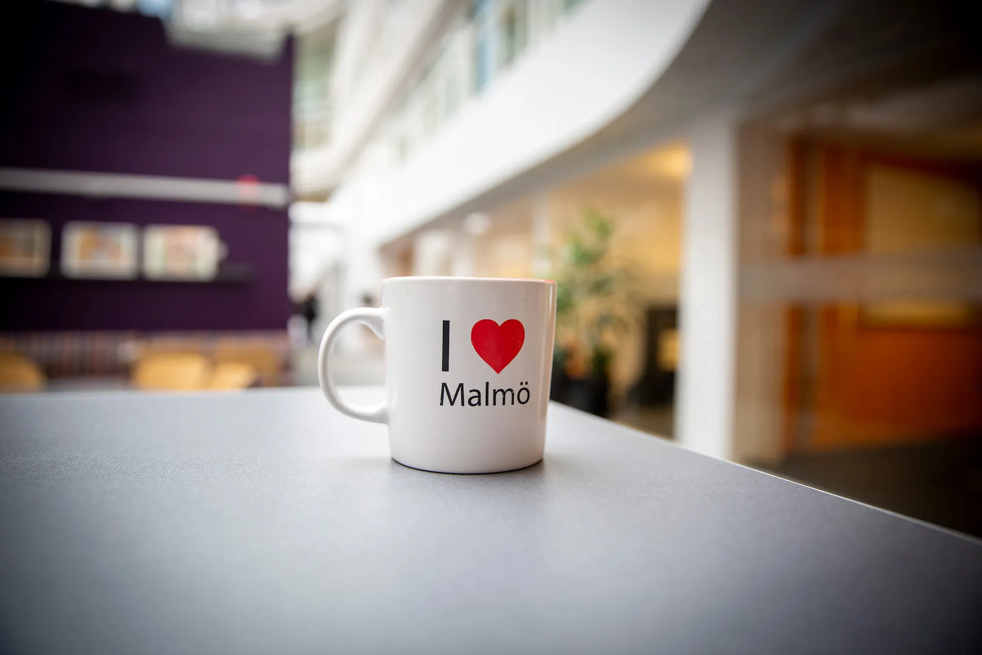 <p>En kaffekopp med texten I Love Malmö mot en lila och vit suddig bakgrund.</p>
