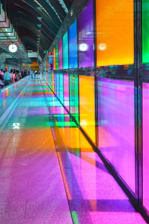 <p>People in a long corridor with different coloured windows.</p>