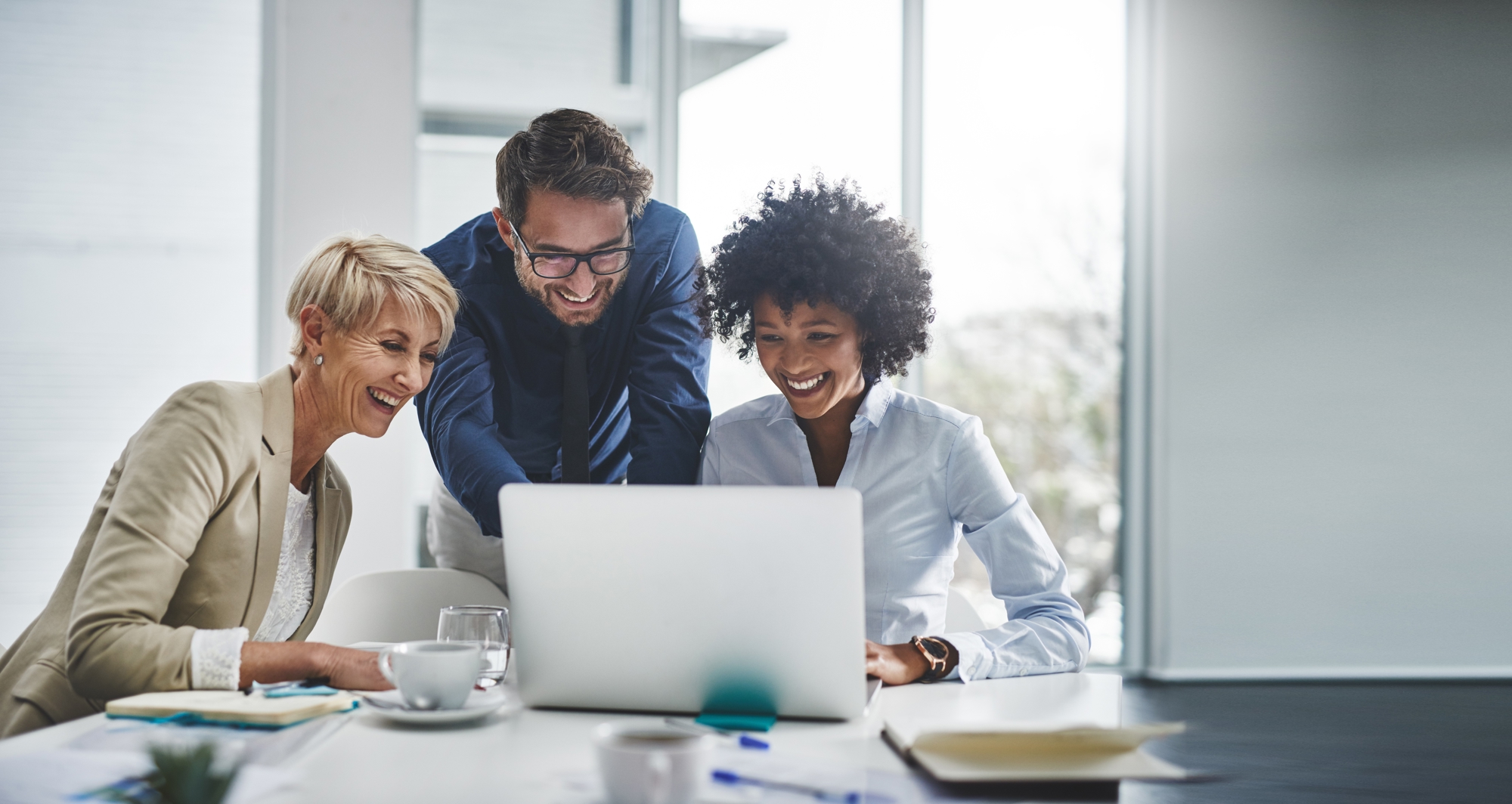<p>Three joyful individuals are gathered around a laptop in an office.</p>