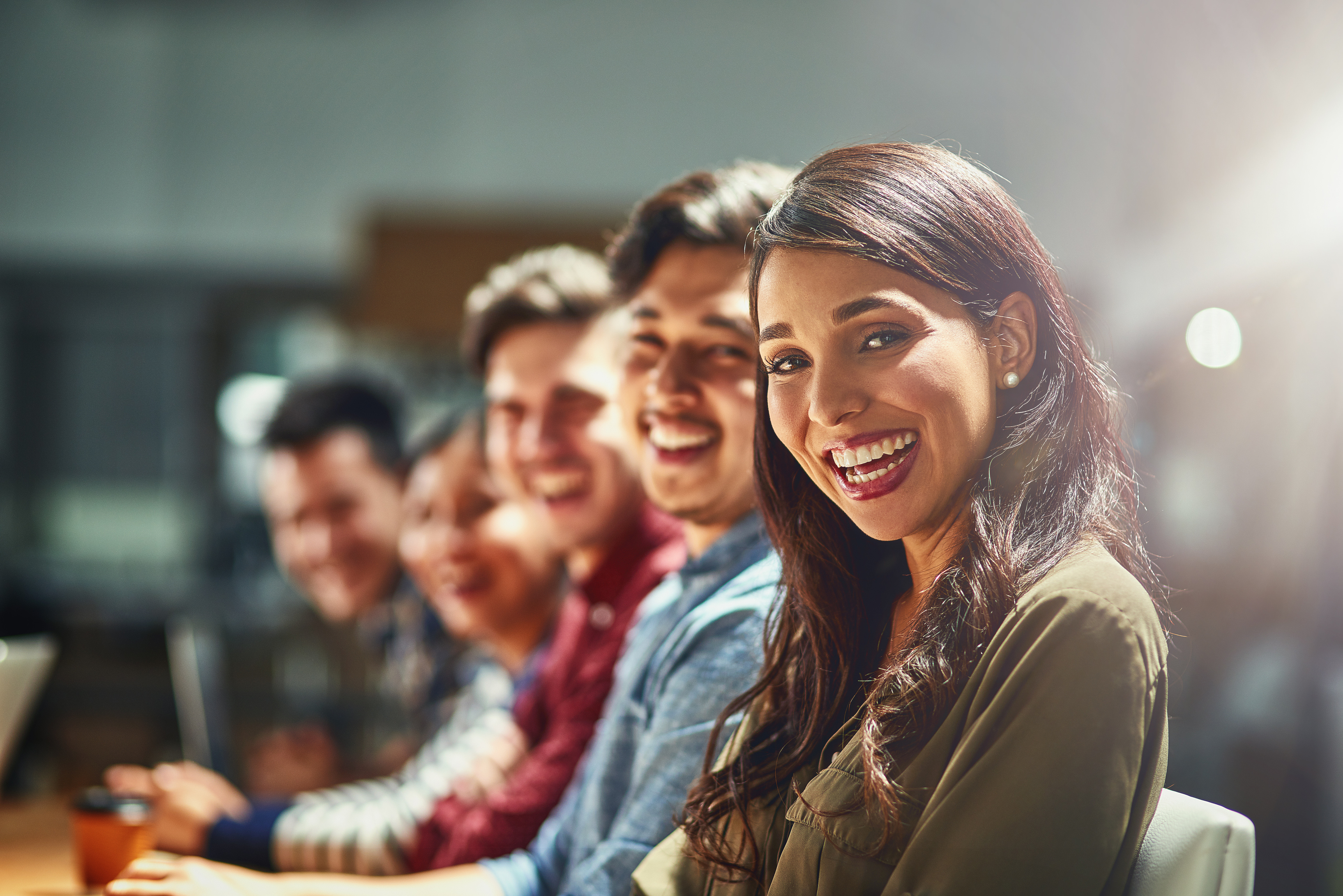 <p>A happy team sitting at a table smiling at the camera.</p>