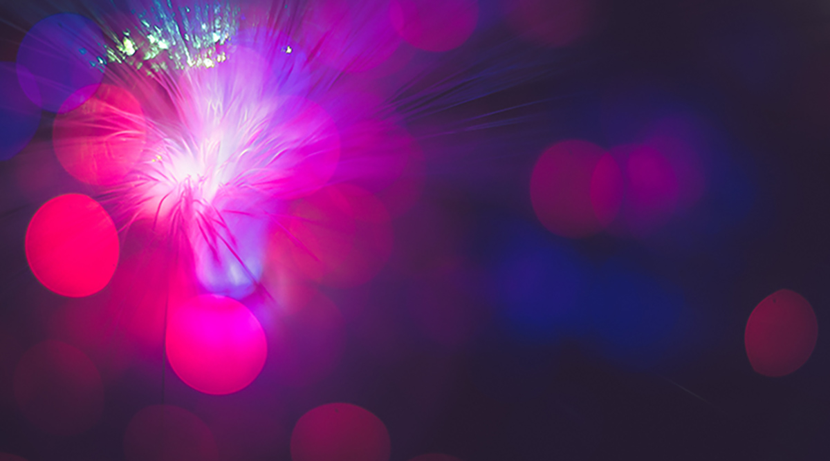 <p>A close-up of a fibre cable with magenta and blue bokeh light.</p>