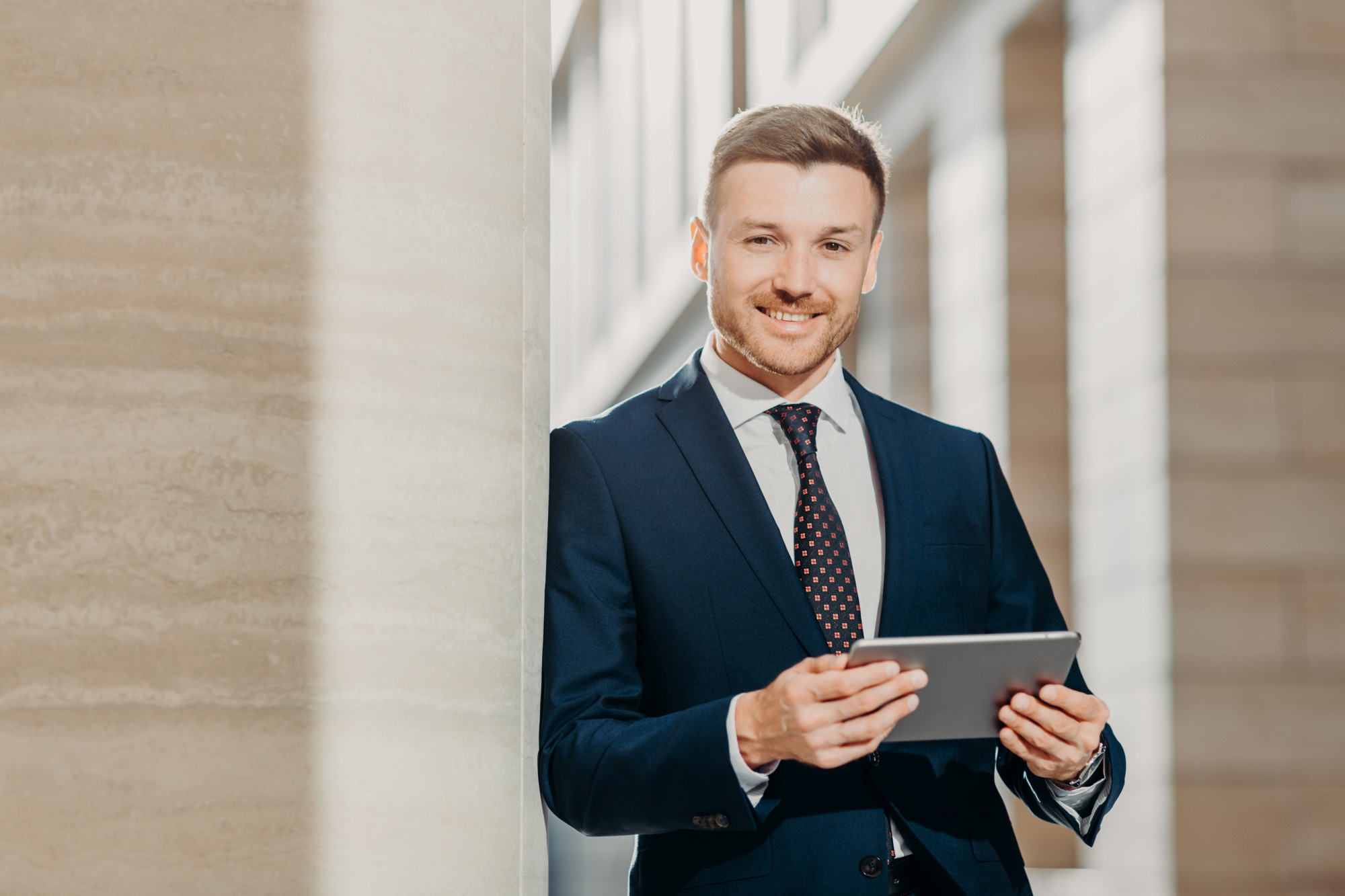 <p>Smiling man holding tablet and looking into camera.</p>