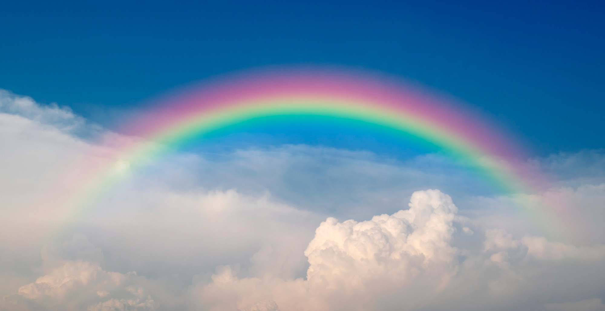 <p>A bright blue sky with a rainbow and some white clouds.</p>