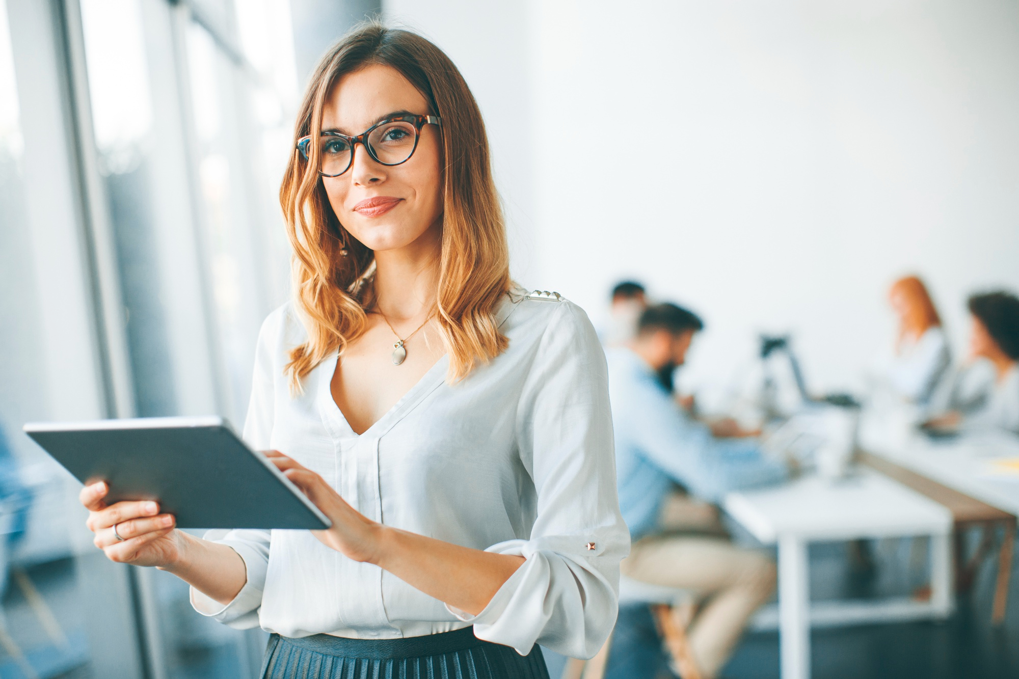 <p>A businesswoman standing in an office environment with a tablet in her hands.</p>