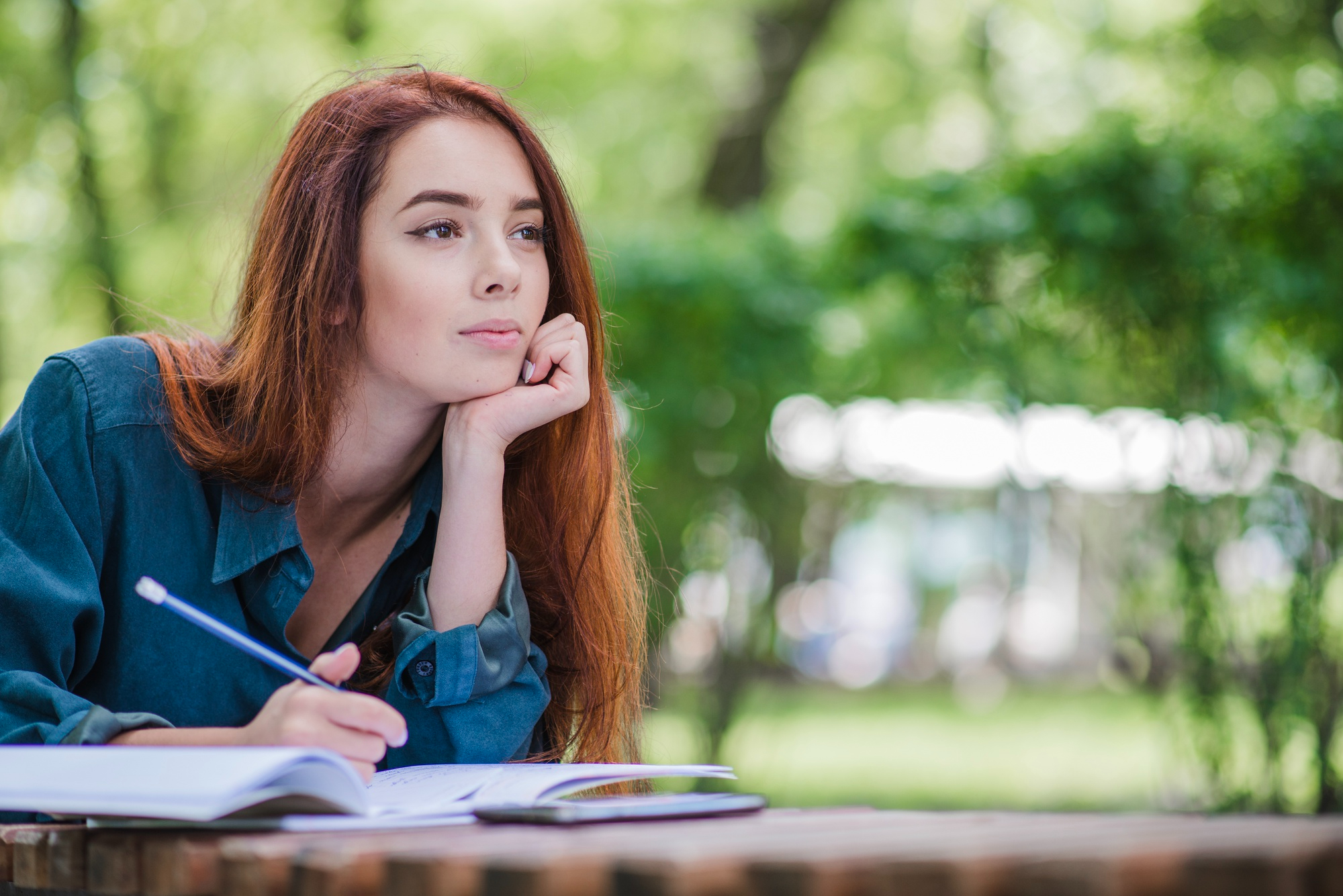 <p>Woman sitting at a table in a park writing.</p>