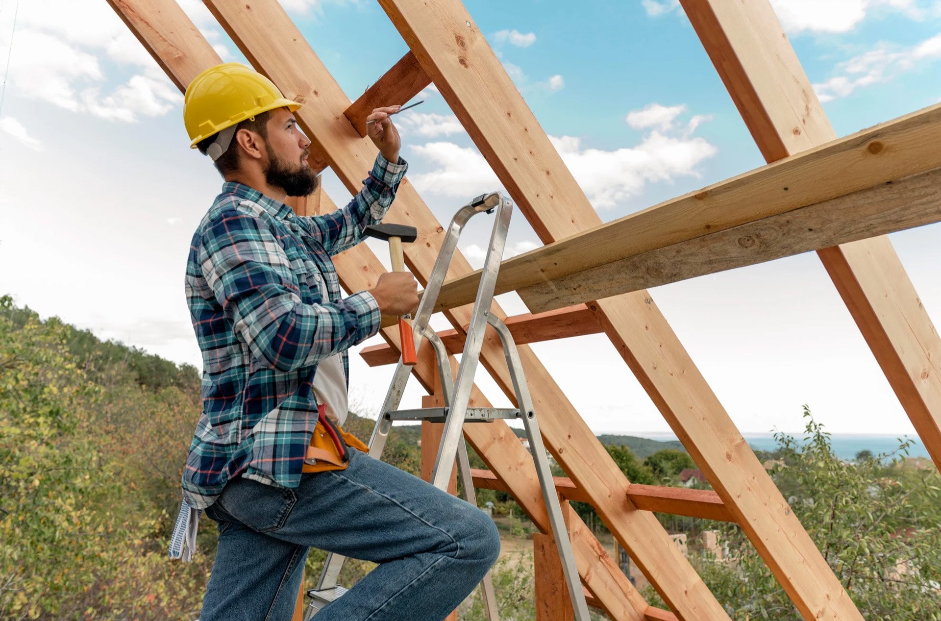 Construction worker on ladder using a hammer while building a wooden roof frame.