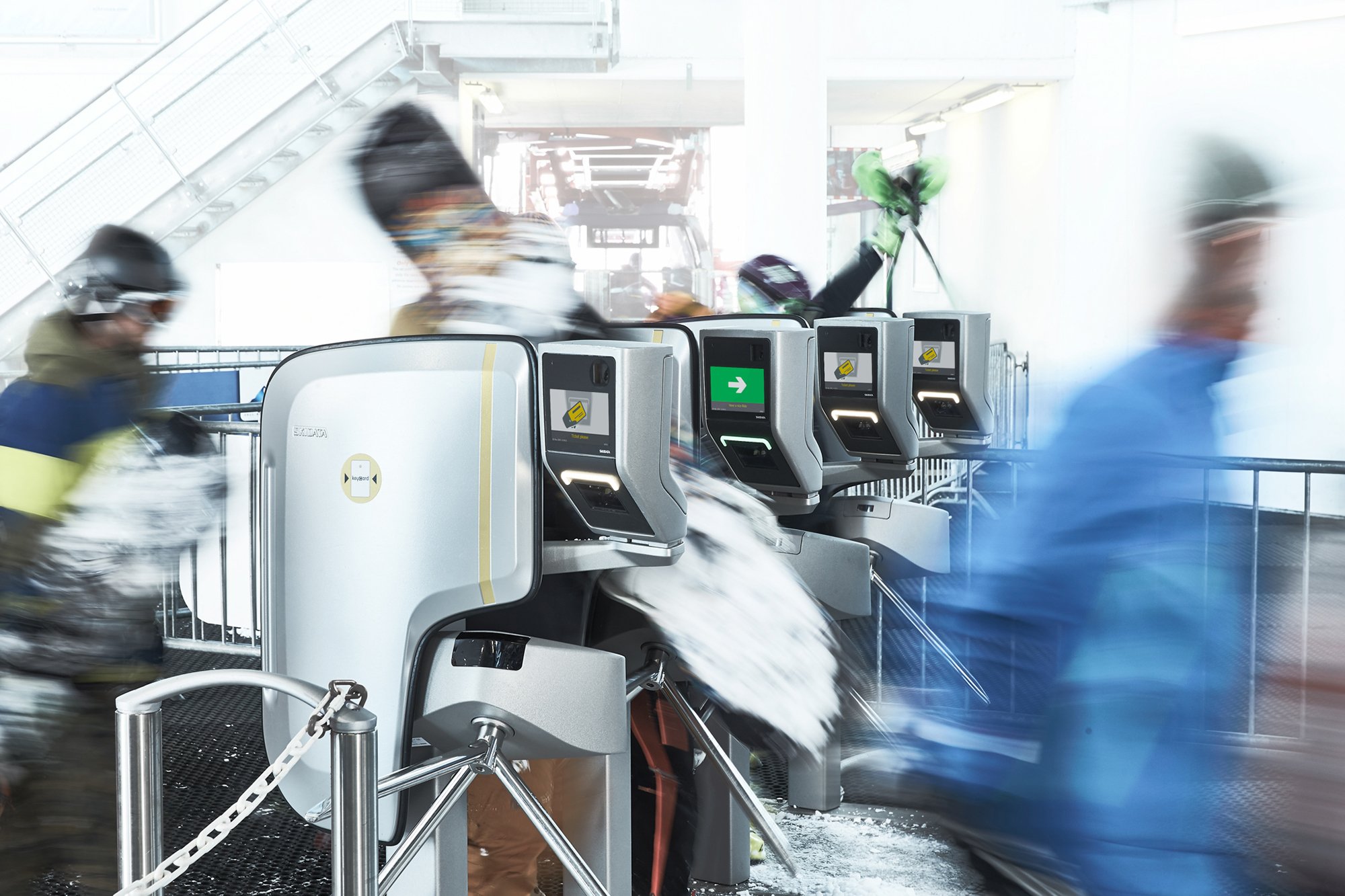 Skiers passing through automated turnstiles at a snowy indoor ski resort entrance.