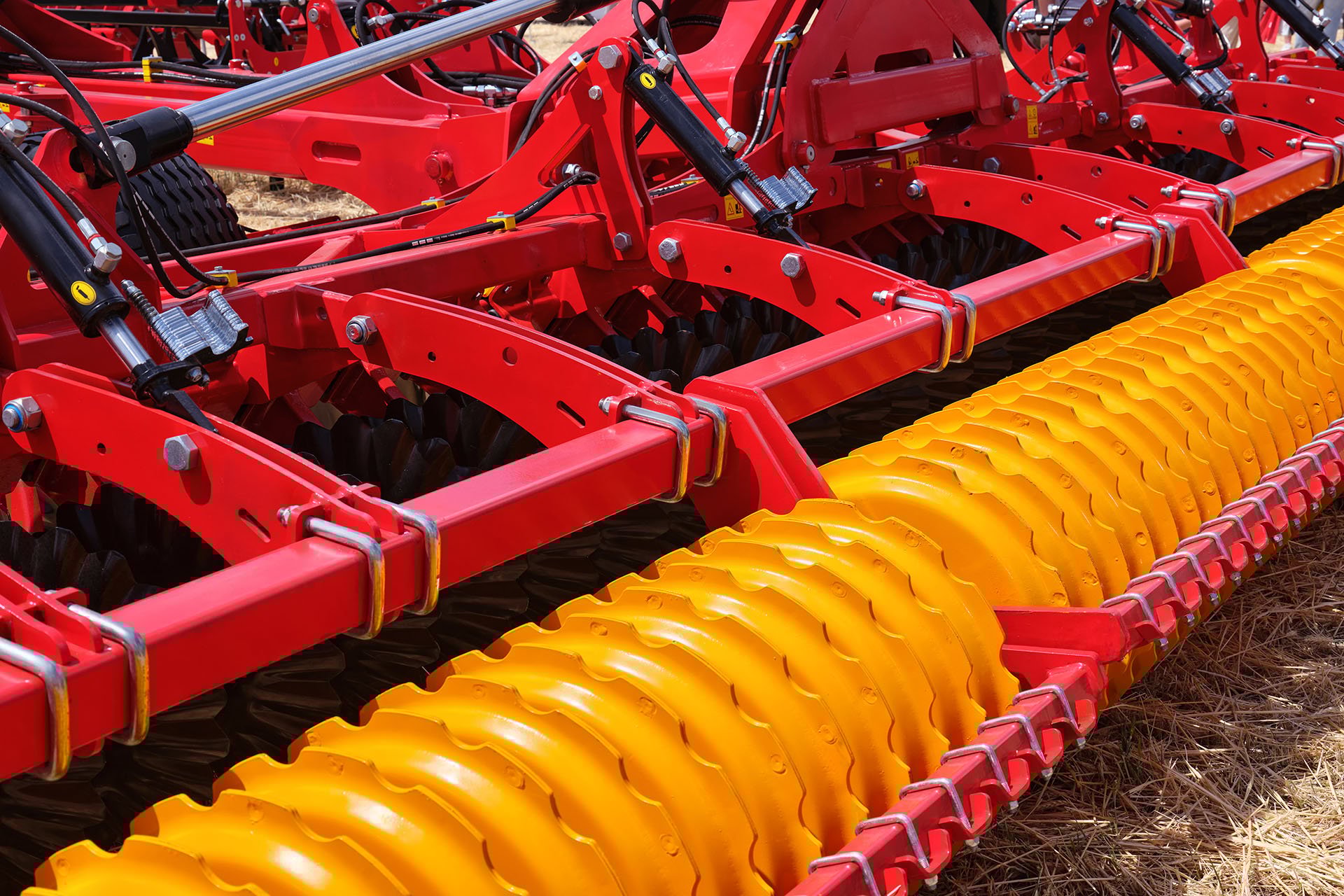 Close-up of a red agricultural implement featuring distinct yellow steel rollers, designed for soil preparation in farming.