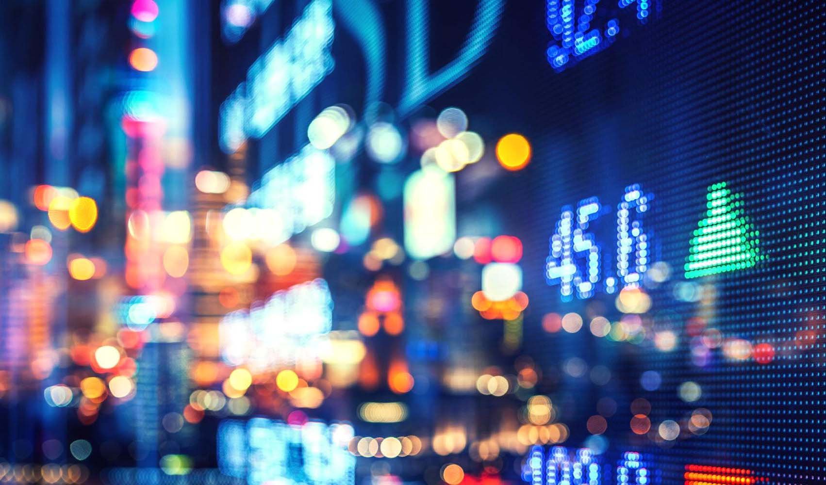 Colorful digital stock market display with numbers and upward green arrow in a city at night.
