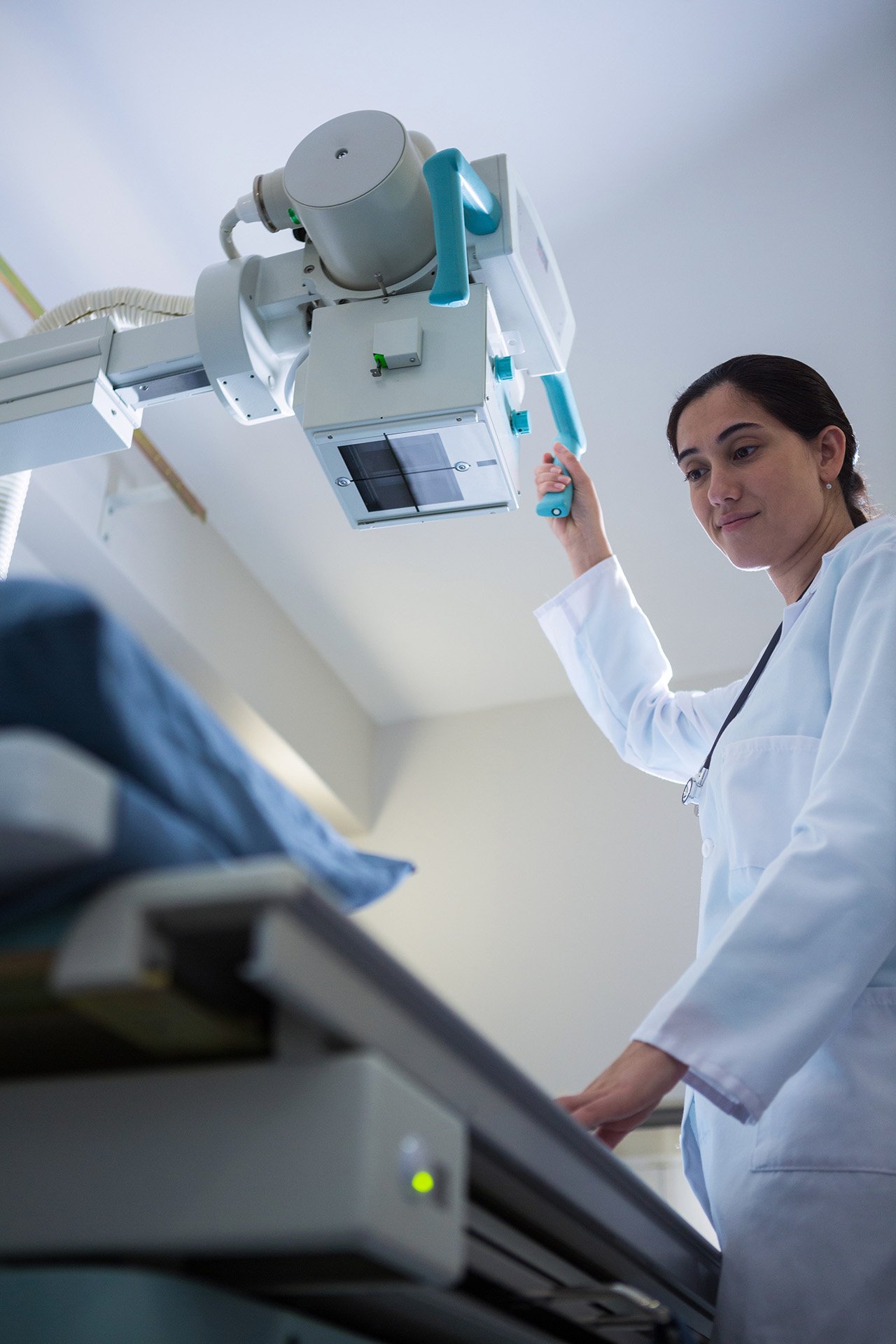 Radiologic technologist adjusting an overhead X-ray machine above a patient table.
