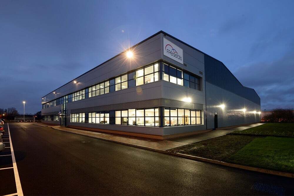 Modern industrial building of FPS Seals illuminated at dusk with parking lot and lights.
