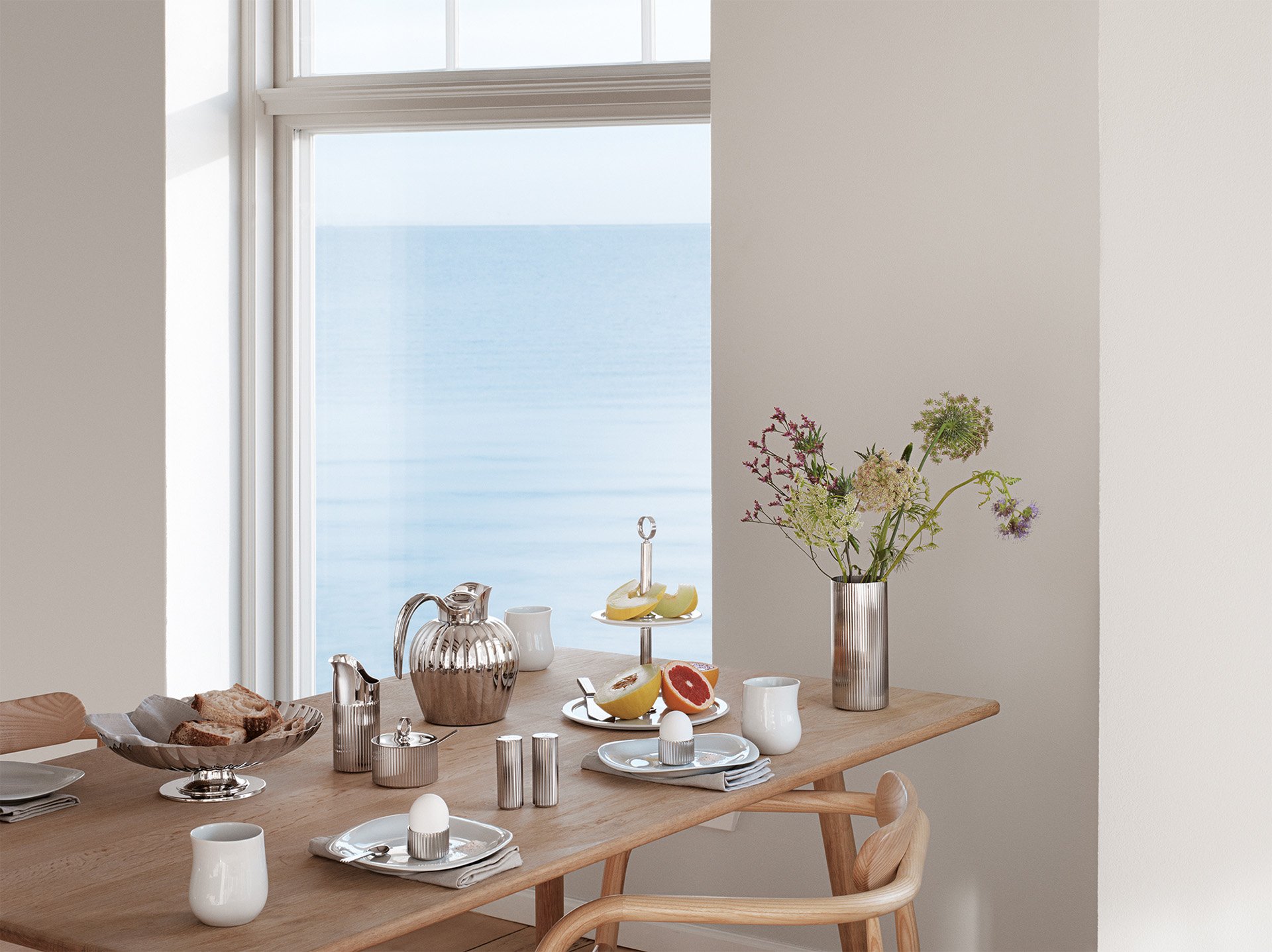 Elegant breakfast table setup with silverware and ocean view through large window.