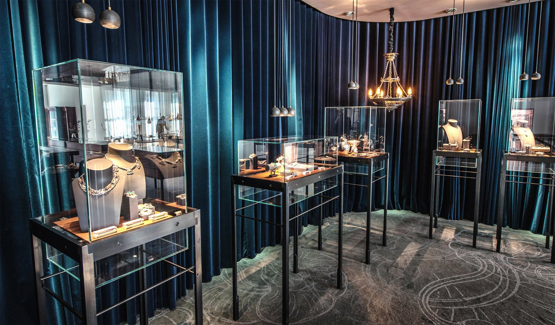 Luxury jewelry display in a dimly lit showroom with blue velvet curtains and glass cases.