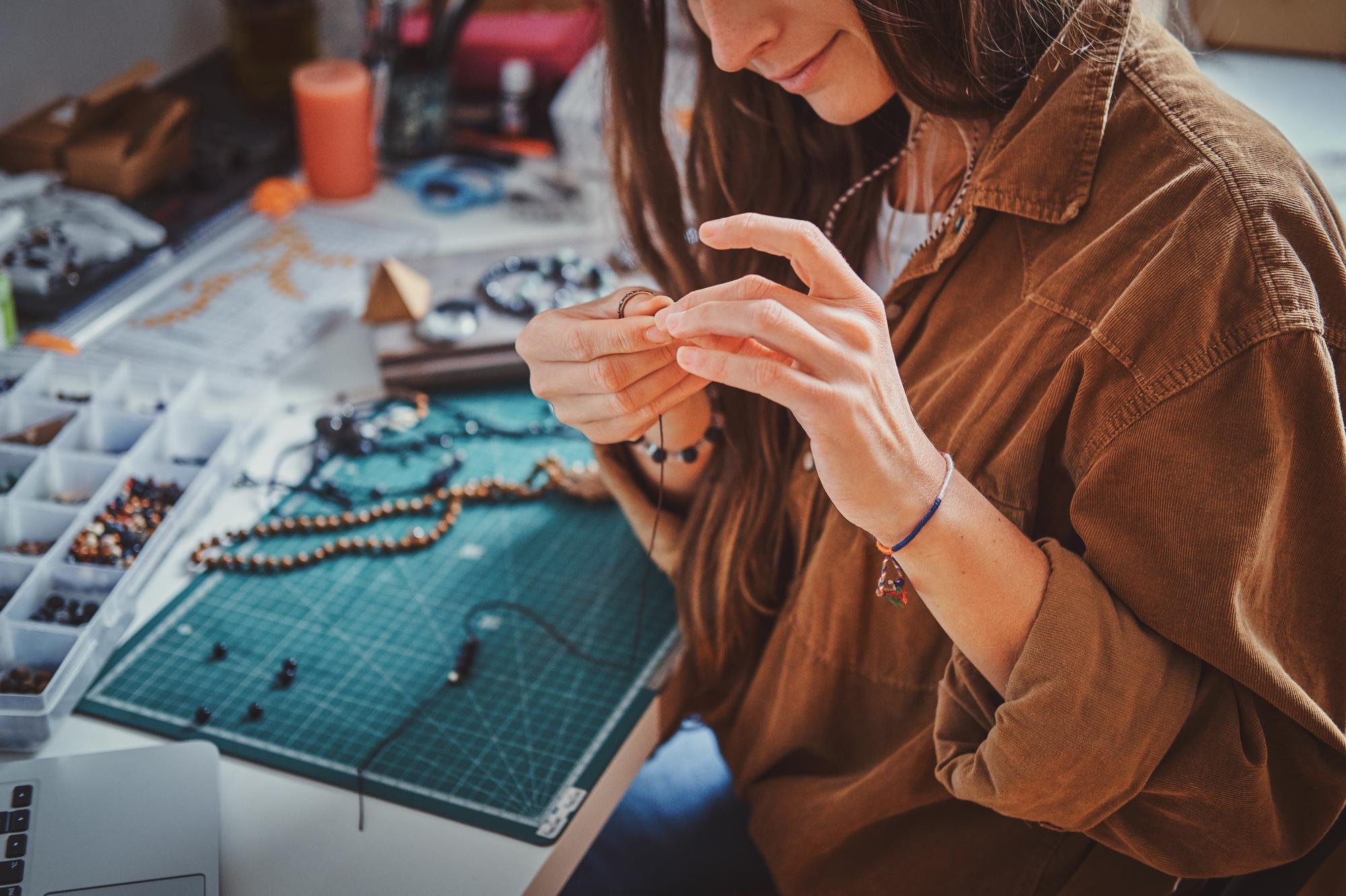 Woman making handmade jewellery with beads at a craft workspace.