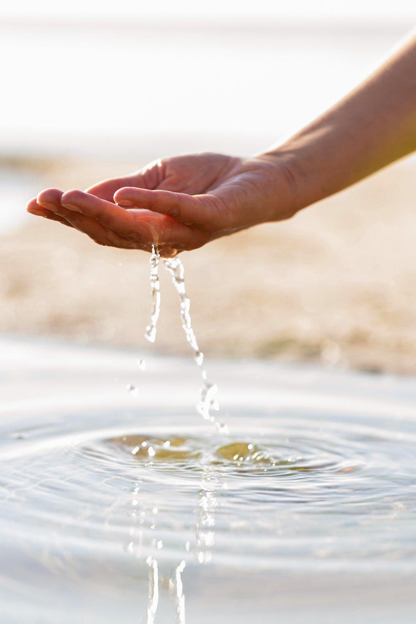 Hand scooping water from a calm surface with ripples and water droplets.