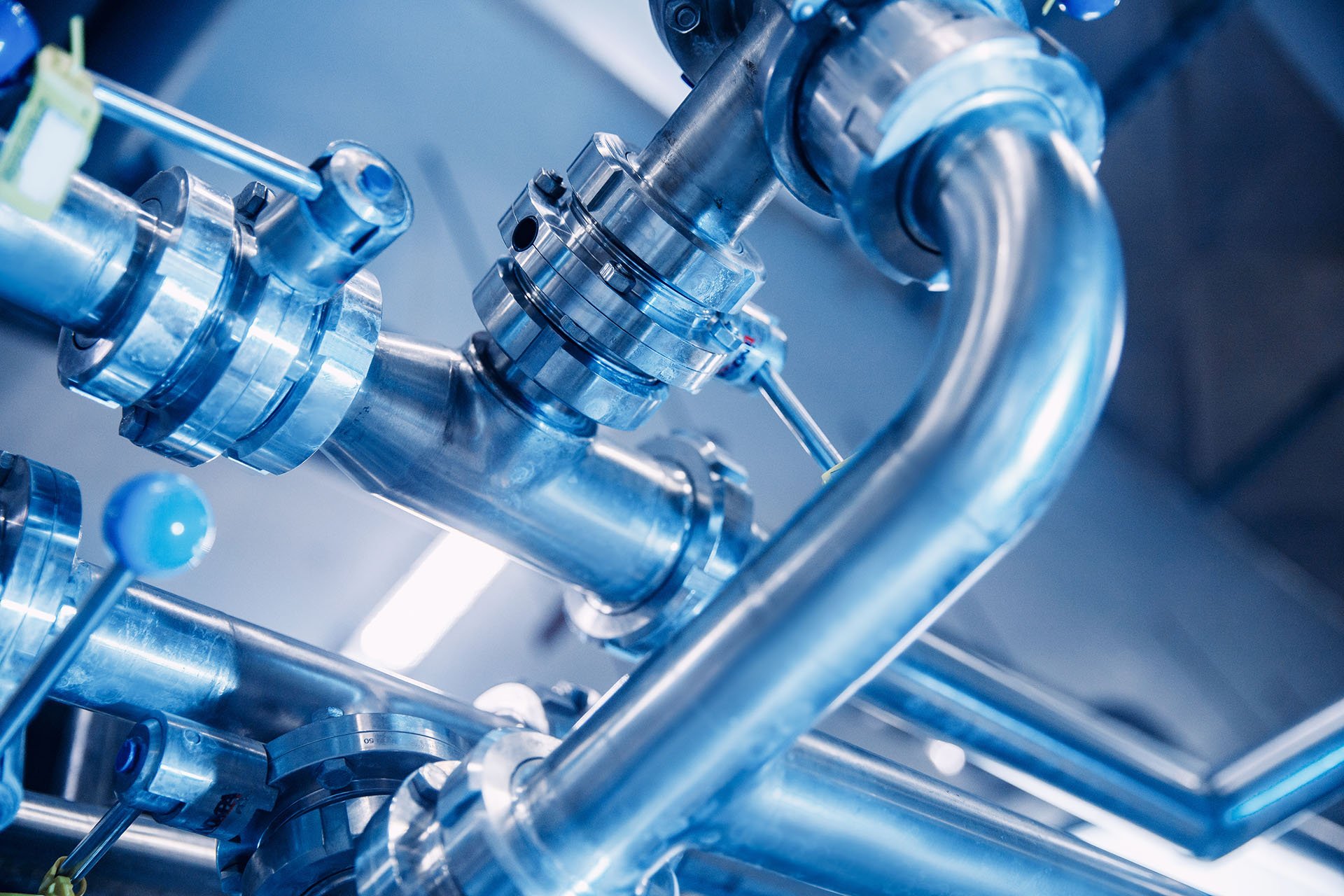 Close-up of shiny stainless steel pipes and valves in an industrial setting, highlighting the intricate connections and machinery.