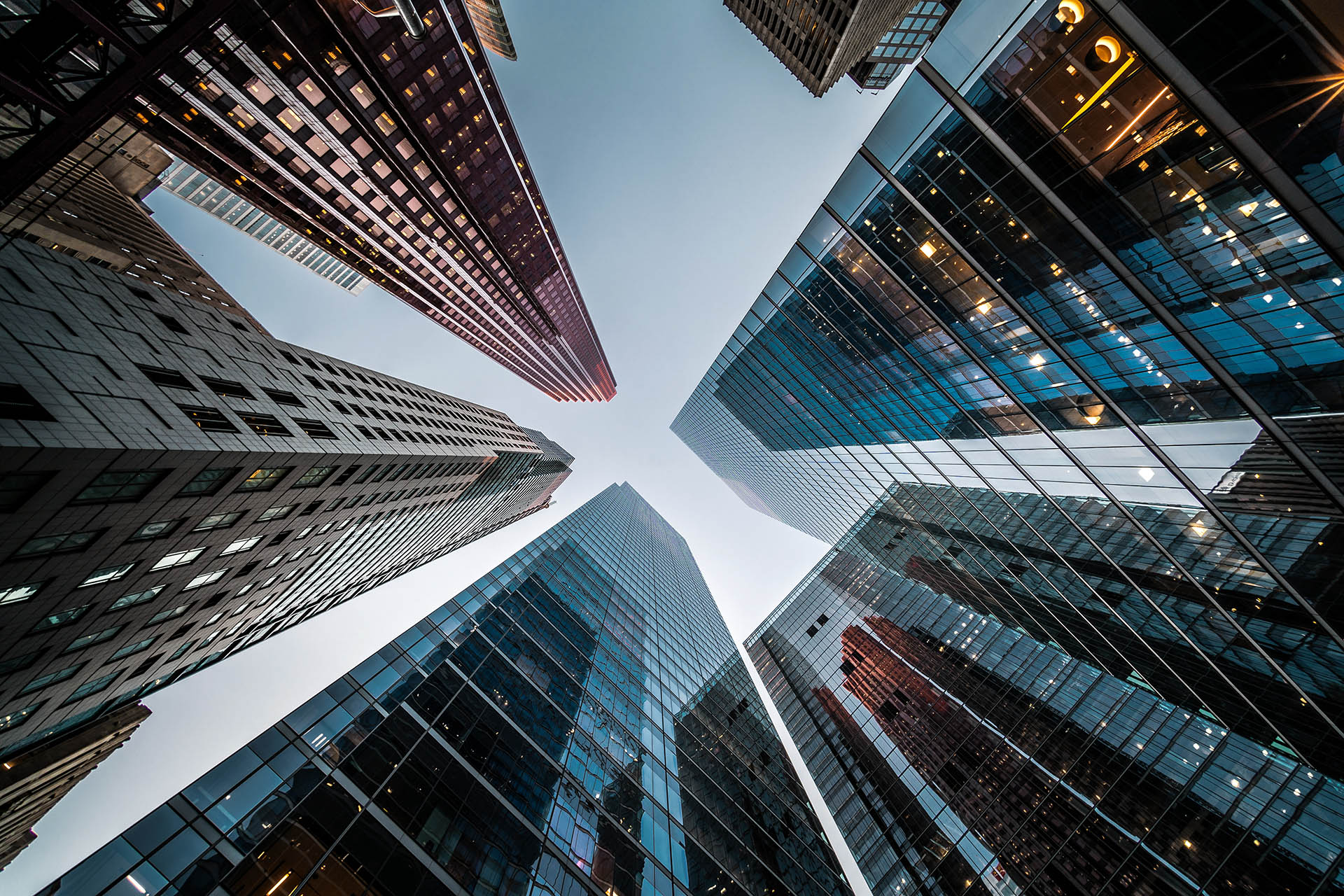 View of several modern skyscrapers shot from below, converging towards the sky, with glass and steel facades reflecting the surrounding buildings.